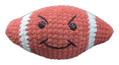 Crochet football with white stripes and a mischievous grin