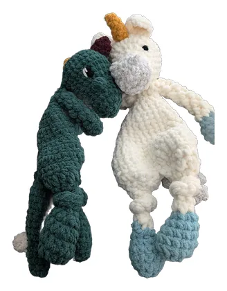 Green dinosaur and white unicorn crochet loveys snuggled together