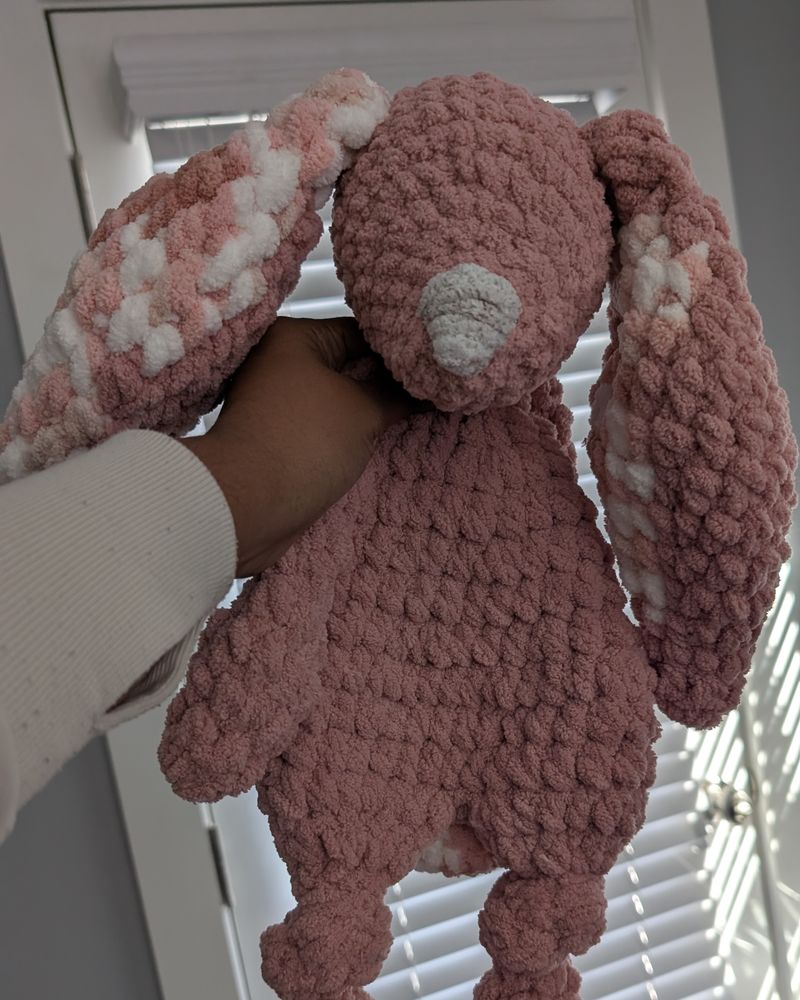 Neelima’s hand holding up a dusty-rose crochet bunny lovey with speckled ears