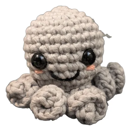Small taupe crochet octopus with big eyes and curled tentacles